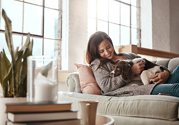 Woman relaxing on couch with dog following tooth extraction 